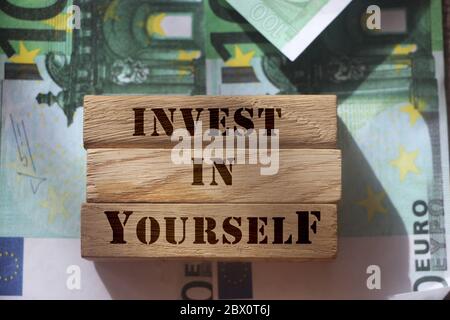 Invest in Yourself, phrase written on vwooden blocks standing on 100 Euro bills. Soft skills and achievements concept. Individual Saving and Stock Photo