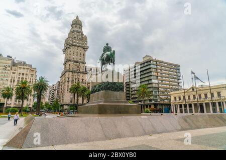 Tourists passing the statue of General Artigas on the Independance square (Plaza Indepencia) with in the background the famous Salvo Palace (Palacio S Stock Photo
