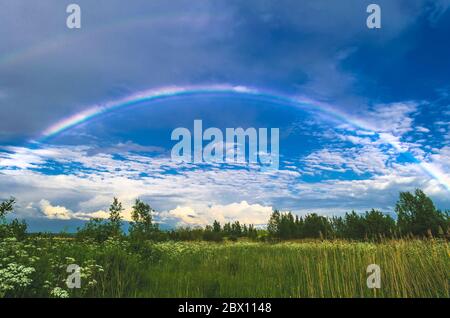Rainbow in the sky over fields and forests after rain Stock Photo