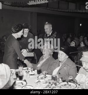 1960s, historical, at an old people's christmas lunch inside the town hall, a surprise for the guests, as a delighted old lady shakes the hands of a Royal visitor, Princess Alice accompanied by the Mayor on a Royal visit to the borough of Lewisham, South London, England, UK. Born in 1885 at Windsor Castle, Princess Alice of Battenberg was the mother of Prince Philip, the husband of the Queen Elizabeth II. Stock Photo