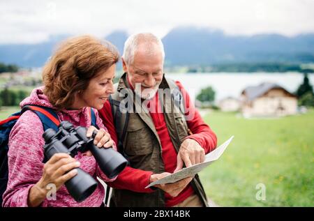 Senior pensioner couple with hiking in nature, using binoculars and map. Stock Photo