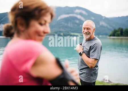 Senior pensioner couple runners with smartphone by lake in nature. Stock Photo