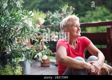 A senior woman sitting outdoors on a terrace, resting after exercise. Stock Photo