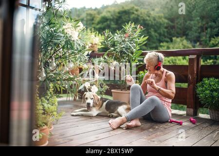 A senior woman with headphones outdoors on a terrace, resting after exercise. Stock Photo