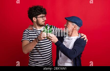 Young man and senior father with bottles in a studio on red background. Stock Photo
