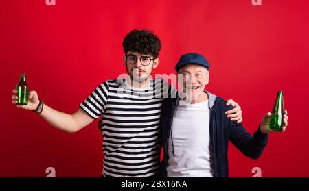 Young man and senior father with bottles in a studio on red background. Stock Photo