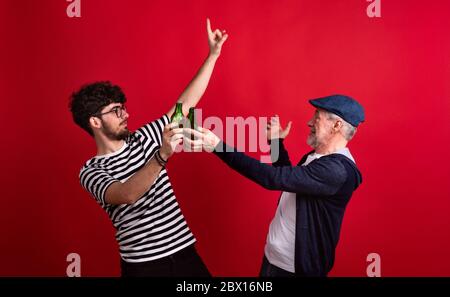 Young man and senior father with bottles in a studio on red background. Stock Photo
