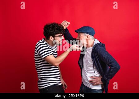 Young man and senior father in a studio on red background, having fun. Stock Photo