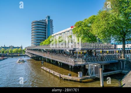 Amsterdam, May 7 2018 - tourist boats on the Prins Hendrikkade with the Ibib Hotel and the big covered bicycle storage building where you can leave yo Stock Photo