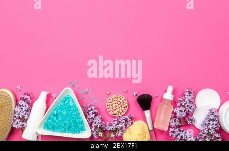 Flat lay view of various white cosmetic and beauty products containers with lilac (Syringa) blossoms on pink studio background. Lower border. Stock Photo