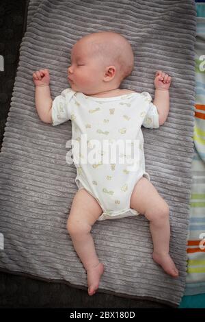 A newborn baby girl sleeping on a grey rug.  Photo by Sam Mellish Stock Photo