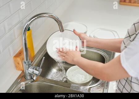Woman hands rinsing dishes under running water in the sink Stock Photo