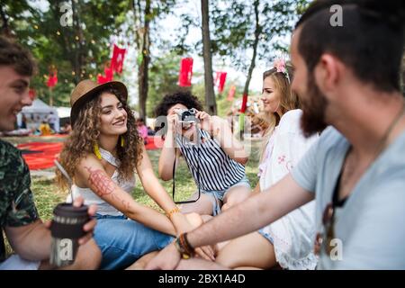 Group of young friends sitting on ground at summer festival, taking photo. Stock Photo