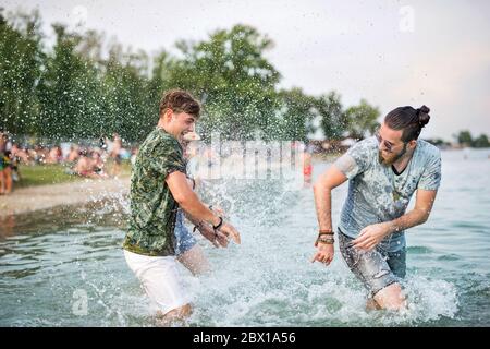 Young men friends having fun at summer festival, standing in lake. Stock Photo