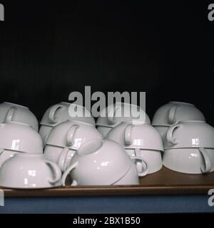 White coffee cups in a cupboard on a shelf on a dark background Stock Photo