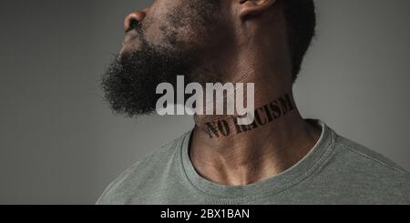Close up portrait of a black man tired of racial discrimination has tattooed slogan no racism on his neck. Concept of human rights, equality, justice, problem of violence, discrimination. Flyer. Stock Photo