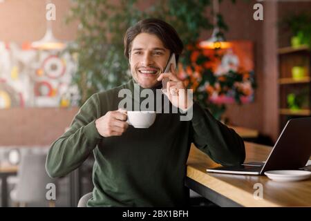 Cheerful young man working with laptop at cafe Stock Photo
