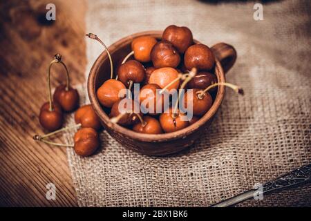 Ripe red organic cherries in a bowl and next to it on wooden table. Sweet cherry berries on old rustic stump. Stock Photo