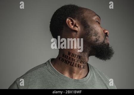 Close up black man tired of racial discrimination has tattooed slogan white silence is compliance on his neck. Concept of human rights, equality, justice, problem of violence and racism. Eyes closed. Stock Photo