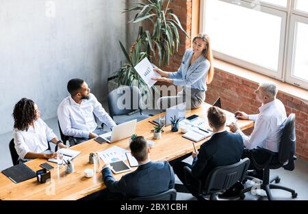 Businesswoman Showing Charts To Colleagues Analyzing Business Effectiveness In Office Stock Photo