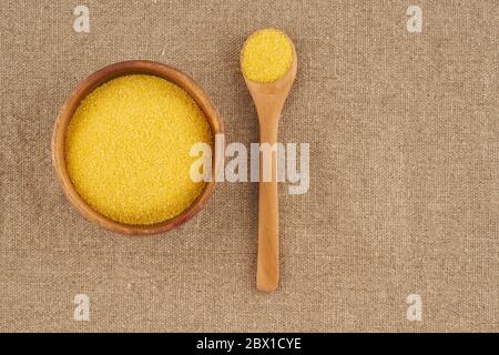 Yellow corn flour in wooden bowl on rustic linen napkin. Ingredients for Polenta Stock Photo