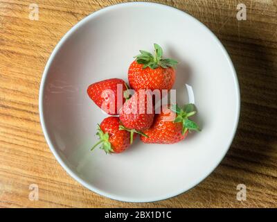 Five fresh strawberries with stalks in a bowl on a wooden board Stock Photo