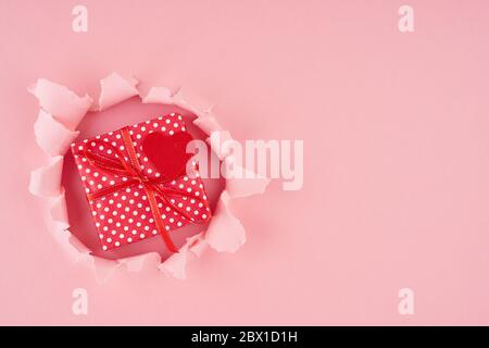 Valentine's Day. A ripped hole and red heart with gift box in bright pink Stock Photo