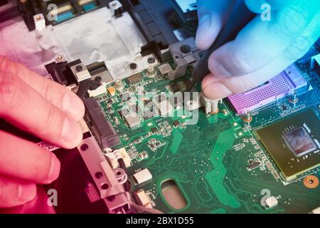 Man repairs computer. A service engineer in shirt repairs laptop, at white Desk Stock Photo