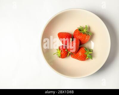 Five fresh strawberries with stalks in a bowl on a white background with copy space Stock Photo