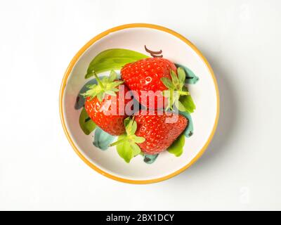 Three fresh strawberries with stalks in a bowl on a white background Stock Photo