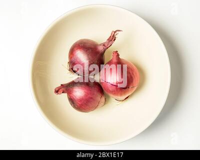 Three small red onions in a bowl isolated on a white background Stock Photo