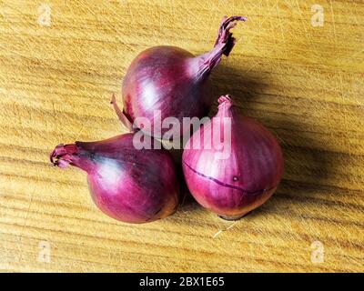 Three small red onions on a wooden chopping board Stock Photo