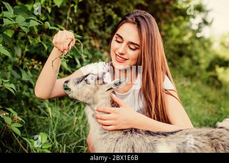 Woman and small goat green grass. Eco farm. Love and care. Animals law. Farm and farming concept. Village animals. Girl play cute goat. Feeding animal. Protect animals. Veterinarian occupation. Stock Photo