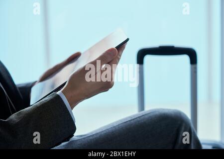 closeup of a young businessman, in a gray suit, sitting in the waiting hall of an airport or a train station, using his digital tablet Stock Photo