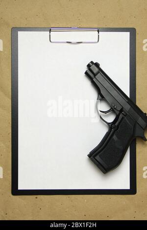 A tablet with a white sheet of A4 format with gun on a beige craft paper. Concept of the legal system, criminal organizations, security services. Stock photo with empty place for your text and design. Stock Photo