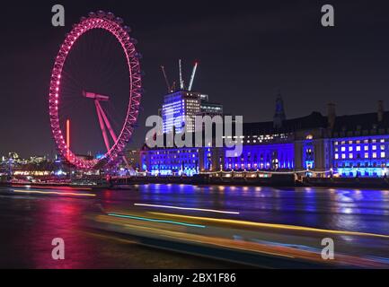 Night time view of the London Eye on the south bank of the River Thames.  Includes light trails from river traffic in the foreground. 11 December 2018 Stock Photo