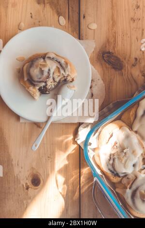 Freshly baked cinnabon buns with cream in a glass dish on a wooden table, top view flat lay Stock Photo