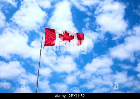 Large Canadian Flag flying proudly with beautiful blue and white sky background. Stock Photo
