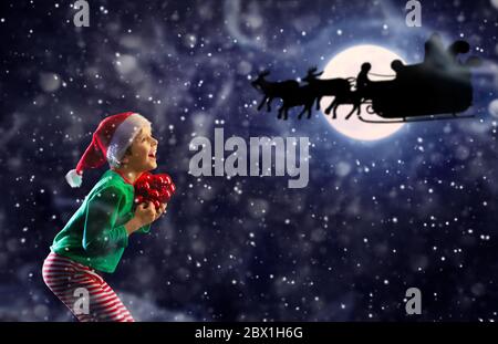 Happy jumping little boy jump from joy with New Year decorations look at silhouette of Santa reindeer sledge over moon Stock Photo