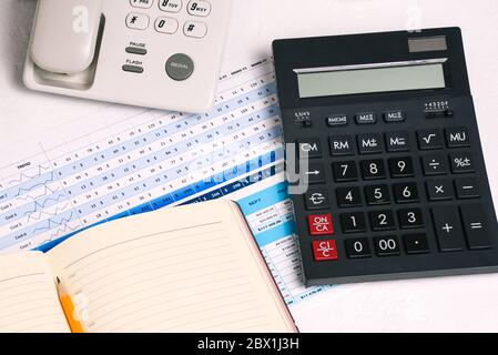 A push-button phone, a calculator, a notebook, and a graph with a table. Financial documents on the employee's Desk. Report for a month or year. Accou Stock Photo