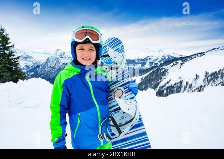 Front portrait of a boy hold snowboard in hands over high mountain peaks panorama Stock Photo