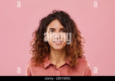 Portrait of young woman with curly hair smiling at camera isolated on pink background Stock Photo