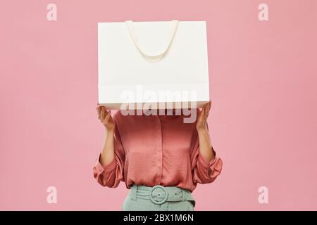 Young woman hiding before the big white shopping bag while standing against the pink background Stock Photo