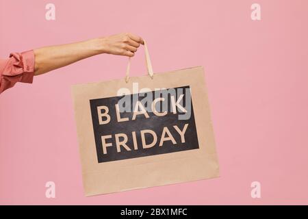 Close-up of female hand holding Black Friday shopping bag against the pink background Stock Photo