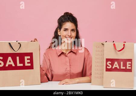 Portrait of beautiful woman with curly hair smiling at camera while sitting at the table with shopping bags Stock Photo