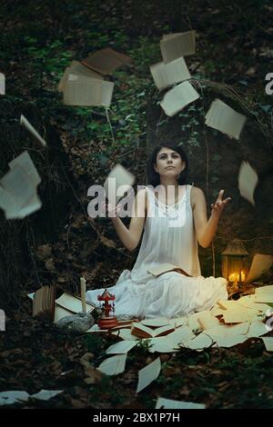 Beautiful woman surrounded by flying pages and books in dark forest. Surreal and weird Stock Photo