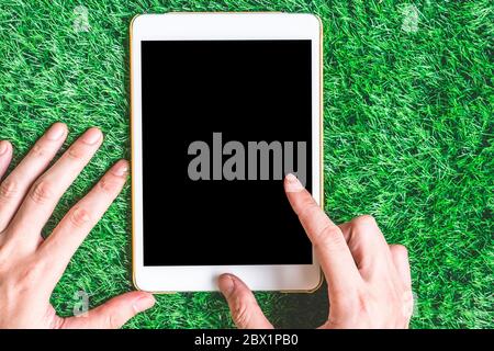 Male hands using blank digital tablet on green grass background. Stock Photo