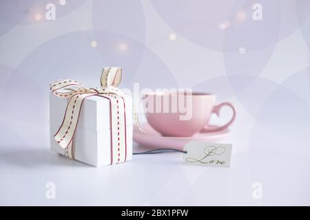 Pink porcelain cup of tea coffee and gift tug with word LOVE on white background with circles. Card, poster, mock up. Celebrating, love, anniversary, birthday, valentins concept. Stock Photo
