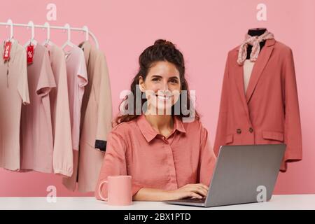 Portrait of young fashion designer sitting at the table and smiling at camera she using laptop computer Stock Photo