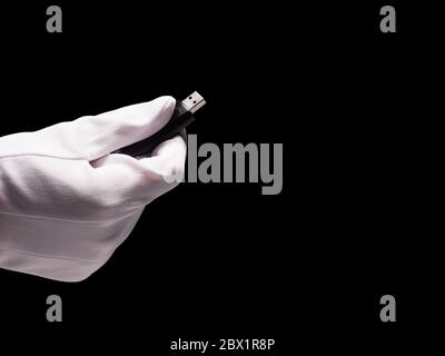 Hand in white glove holding usb flash drive on black background. Free space for text Stock Photo